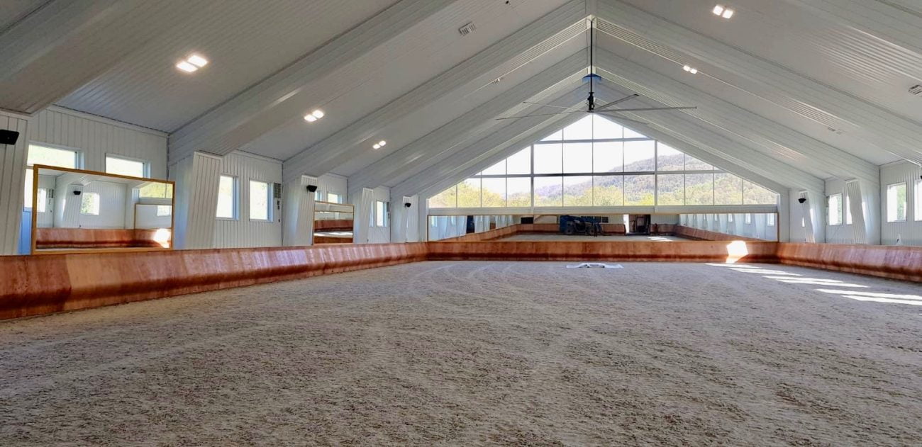 An indoor arena with a natural wood colored curved kickwall, with bright white walls, high ceilings, and natural light.