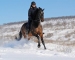 A horse and rider canter through the snow outside