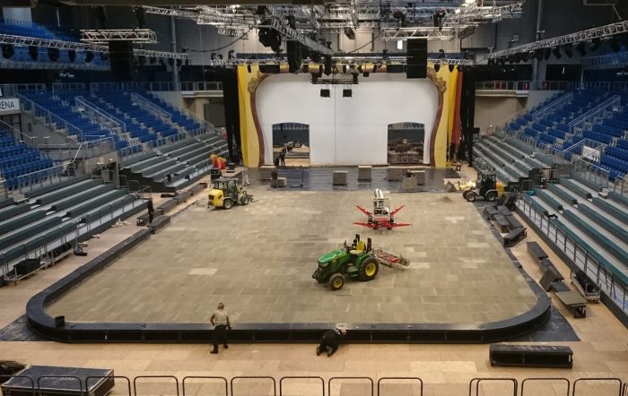 An indoor show arena with grandstands is seen being built with arena mats as the base
