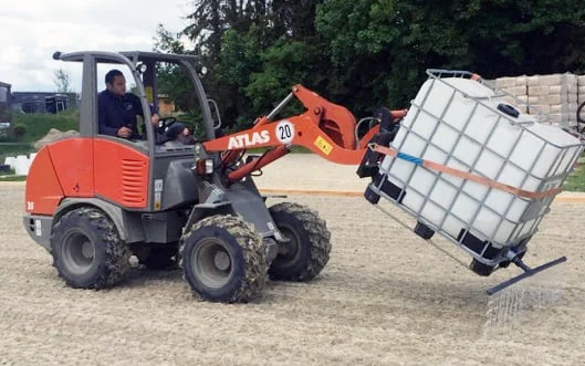 A tractor spreads Hydro SandBinder in a sand arena