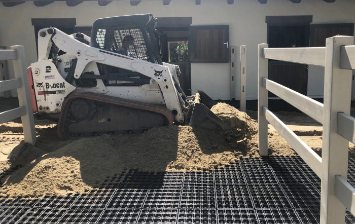 Paddock mats are being covered with sand by heavy machinery.