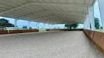 A covered arena with metal roof panels with the wooden safety kick wall in contract and nicely groomed footing