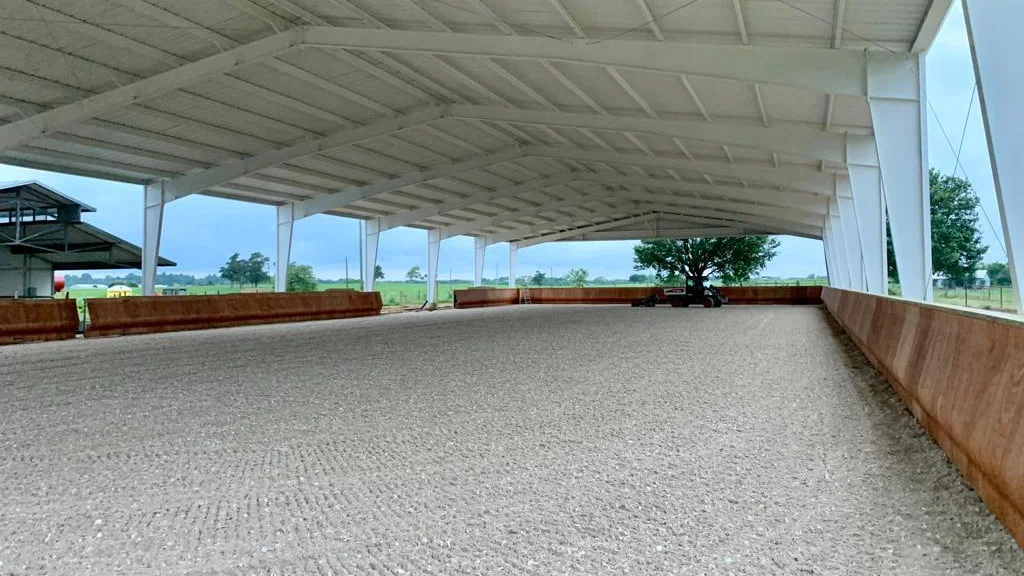 A covered arena with metal roof panels with the wooden safety kick wall in contract and nicely groomed footing