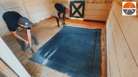 Two people dragging a softbed comfort mat into a stall