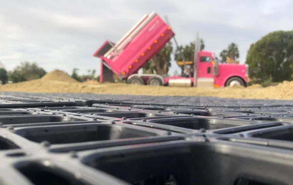 A closeup of a HIT draingrid with a pink work truck dumping sand for the arena in the background