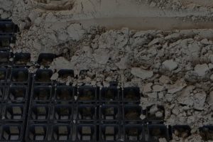 A cropped and darkened photo of HIT draingrids partially covered with sand.