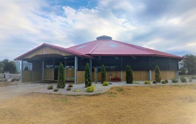 A fully covered horse walker with red roof and a gravel walkway surrounding it
