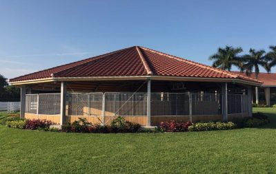 A fully covered round horse walker with reddish brown shingles on the roof and surrounded by flowers