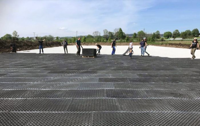 A group of people installing arena mats in a half-finished outdoor arena