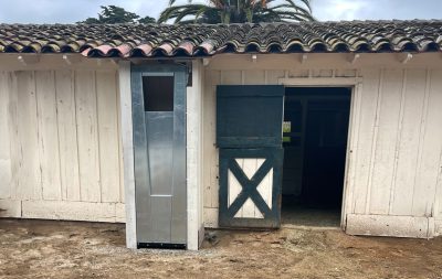 A single automatic feeder integrated into the side of a barn, next to an open stall door
