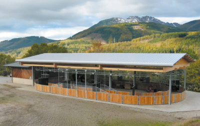 An oval, covered horse walker, with beautiful mountains set in the background