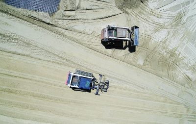 An aerial view of construction equipment spreading and evening sand in an outdoor arena.