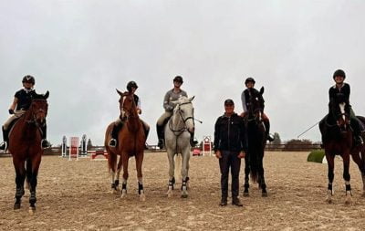 Five horses and riders, with one person standing on the ground pose for a picture in the new outdoor jumping arena at Corralitos Riding Club.