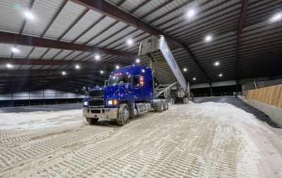 A blue construction truck drops sand in the covered arena in Pilot Point.