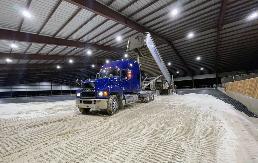 A blue construction truck drops sand in the covered arena in Pilot Point.