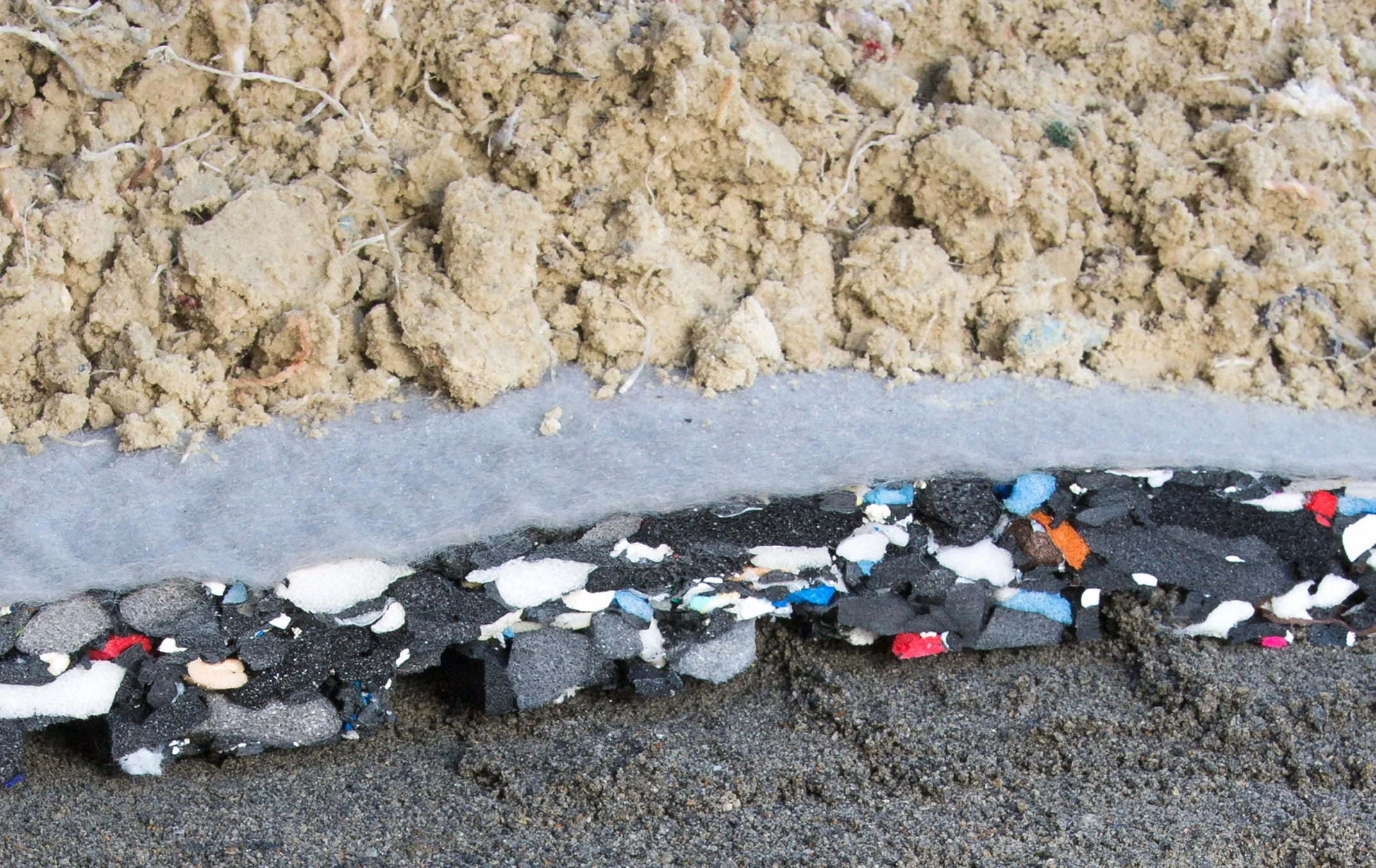 A photo showing the layers of a riding arena with an arena base mat - the ground base, arena mat, and sand.