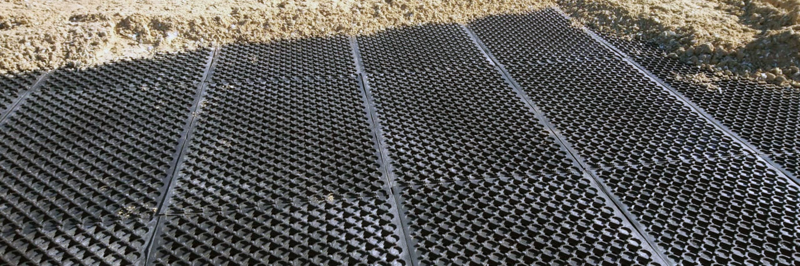 Arena Mats laid in an undefined space, with sand over the top of some mats