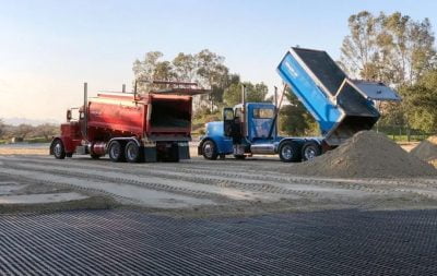 A blue construction truck dumps sand with a red construction truck is parked next to it while building an outdoor arena