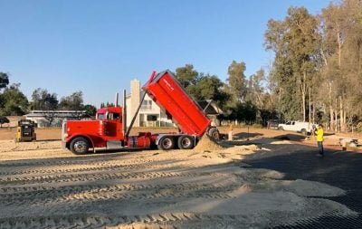 A red construction truck drops sand in a new outdoor arena.