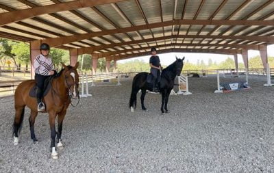 Two horses and their riders stand posing in the new covered jumping arena at North Peak Equestrian.