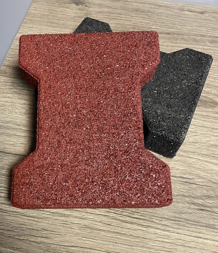 One red rubber paver laying across a black rubber paver, displayed on a wooden table.